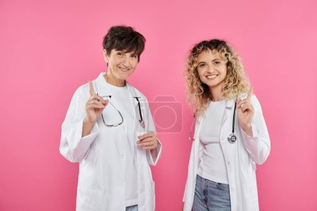 female doctors in white coats warning on pink backdrop, smile, breast cancer awareness, women