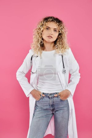 breast cancer awareness concept, curly female doctor looking at camera, pink backdrop, happy woman