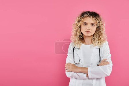 Brustkrebs-Aufklärungskonzept, lockige Ärztin, die in die Kamera schaut, rosa Hintergrund, Frau