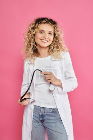 Photo for Breast cancer awareness concept, happy female doctor holding stethoscope, pink backdrop, woman - Royalty Free Image