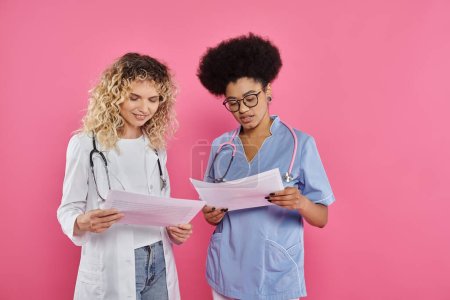 Foto de Oncólogos femeninos felices, doctores interracial en el telón de fondo rosado, conocimiento del cáncer de pecho, diagnóstico - Imagen libre de derechos
