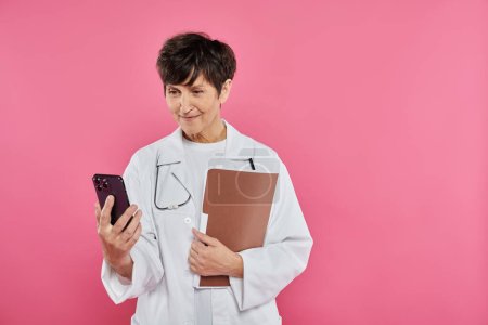 mature oncologist, female doctor holding folder, using smartphone, breast cancer awareness concept