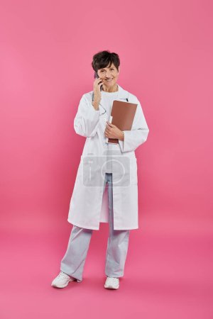 female oncologist, mature doctor holding folder and talking on smartphone, breast cancer awareness