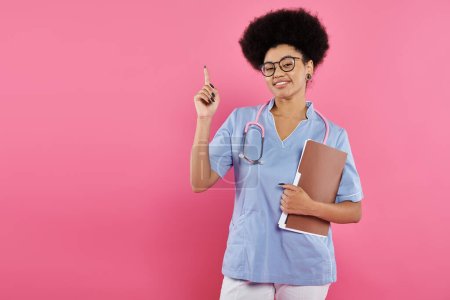 Photo for Breast cancer awareness, african american doctor, happy oncologist with folder, pointing up, pink - Royalty Free Image