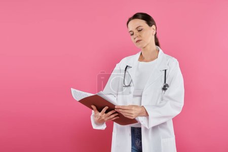Photo for Breast cancer awareness, female doctor, oncologist reading medical record, folder, pink backdrop - Royalty Free Image