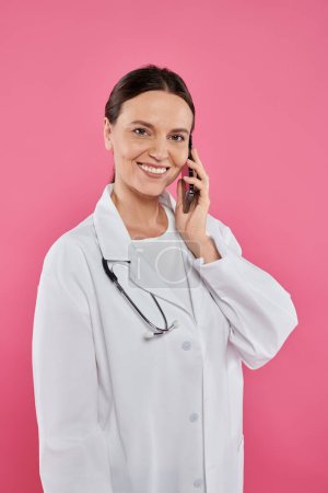 Lächelnde Ärztin spricht auf Smartphone isoliert über pinkfarbenes Brustkrebskonzept