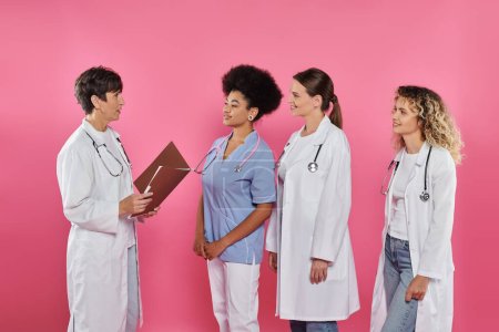Arzt hält Papiermappe neben lächelnden Kollegen auf rosa, Brustkrebs isoliert