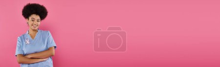 Photo for Smiling african american doctor with ribbon crossing arms isolated on pink, breast cancer, banner - Royalty Free Image
