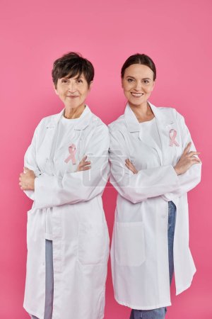 doctores sonrientes con cintas cruzando brazos aislados en rosa, conciencia del cáncer de mama