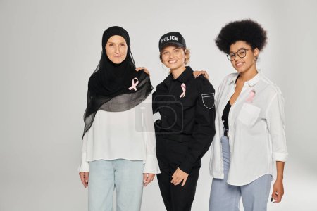 mujeres interraciales positivas y diferentes con cintas rosadas de cáncer de mama aisladas en gris