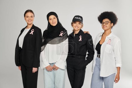 Photo for Smiling different interracial women with pink ribbons of breast cancer standing isolated on grey - Royalty Free Image