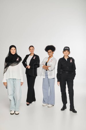 Foto de Feliz multiétnico diferentes mujeres con cintas de conciencia de cáncer de mama en fondo gris - Imagen libre de derechos
