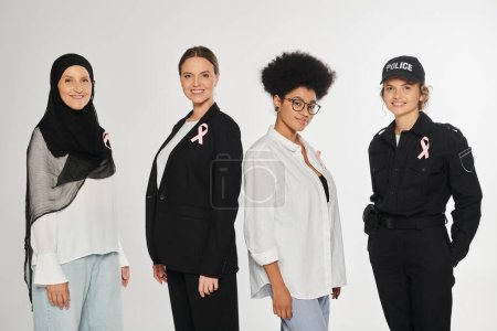 mujeres interracial positivas con cintas de conciencia sobre el cáncer de mama posando aisladas sobre gris