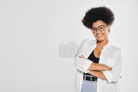 cheerful african american woman crossing arms and looking at camera isolated on grey