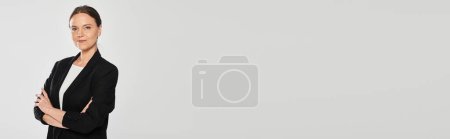 Photo for Confident woman in suit crossing arms and looking at camera isolated on grey, banner - Royalty Free Image