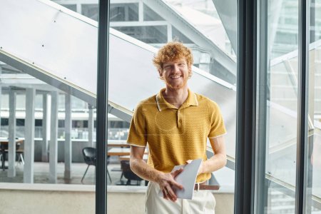 young red haired man in smart casual attire with documents smiling looking at camera, coworking