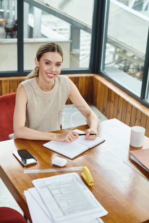 young female employee working with documents at table looking at camera, coworking concept