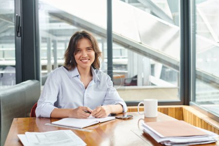 attractive brunette woman in business casual attire smiling and looking at camera, coworking