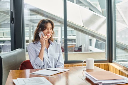 fröhliche junge Angestellte im Business Casual Outfit sitzt und telefoniert, Coworking-Konzept