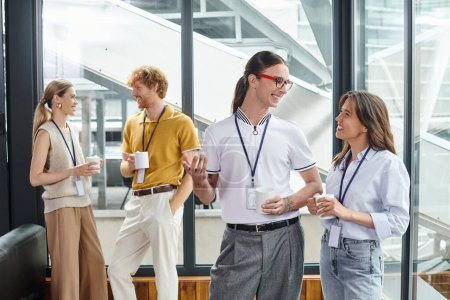 cuatro compañeros de trabajo alegres en ropa inteligente sonriendo entre sí en la pausa del café, concepto de coworking