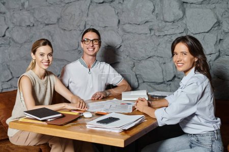 three cheerful coworkers in smart casual outfits working on documents looking at camera, coworking