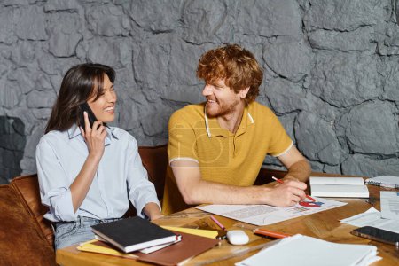 young cheerful colleagues working and talking on phone smiling to each other, coworking concept