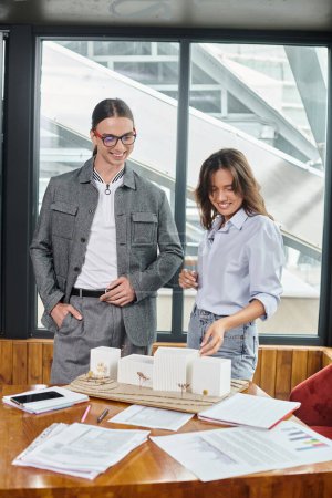 creative team members in smart casual wear discussing scale model and paperwork, design bureau