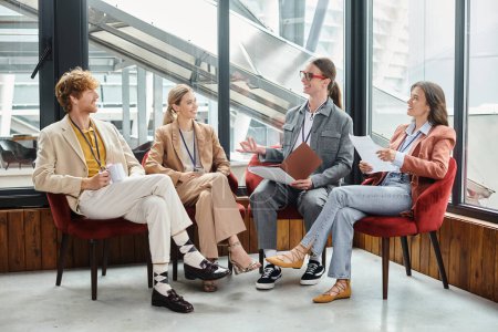 junges Team in Business-Casual-Kleidung sitzt und diskutiert mit Papieren, Coworking