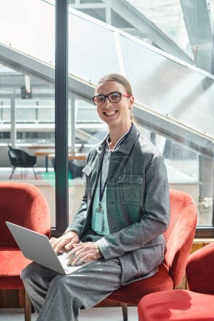 Photo for Smiling young employee with glasses looking at camera while working on his laptop, coworking - Royalty Free Image