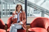 cheerful brunette employee sitting on chair and drinking beverage while on break, coworking concept puzzle #673736296
