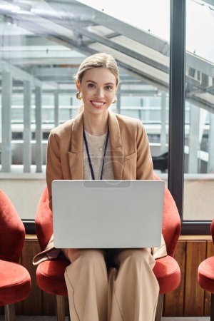 Nahaufnahme einer jungen Frau im schicken Anzug, die an ihrem Laptop arbeitet und in die Kamera schaut, Coworking-Konzept