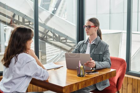 zwei Coworker sprechen über ihre Arbeit mit Laptop und Papieren auf dem Tisch, Coworking-Konzept