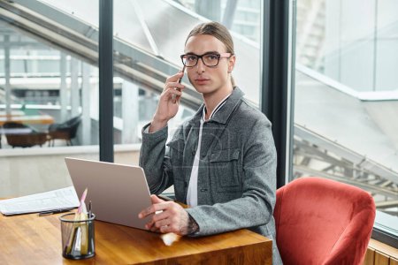 young handsome worker looking at camera while working and talking on phone, coworking concept