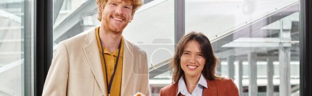 two cheerful team members smiling and looking at camera with glass on backdrop, coworking, banner