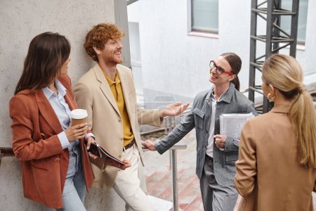 equipo alegre en elegante ropa inteligente discutiendo su trabajo y sonriendo durante el descanso, coworking