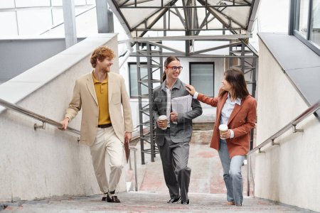 drei junge Kollegen gehen die Treppe hinauf und lächeln aufrichtig, Hand in Schulter, Coworking-Konzept