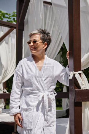 glückliche reife Frau mit Sonnenbrille, die sich im privaten Pavillon ausruht, Wellness-Rückzugsort im Luxus-Resort