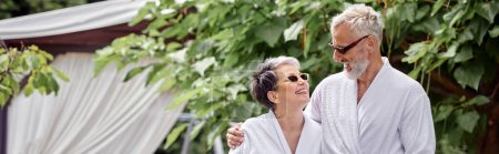 alegre hombre maduro con tatuaje abrazando esposa en gafas de sol y bata, jardín de verano, pancarta