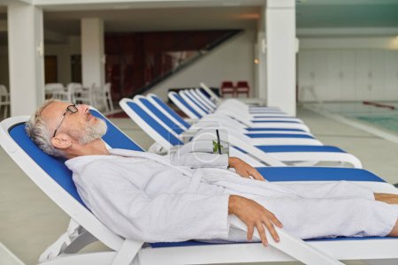 Photo for Wellness retreat concept,  mature man in white robe resting on lounger near cocktail in spa center - Royalty Free Image