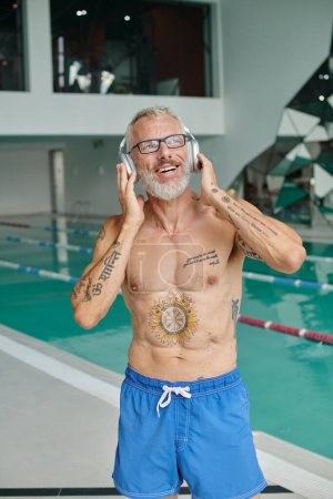 Foto de Terapia musical, hombre de mediana edad tatuado escuchando música en auriculares inalámbricos en el centro de spa - Imagen libre de derechos