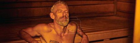 homme d'âge moyen tranquille, détendu et torse nu avec tatouages assis dans le sauna, bien-être, bannière