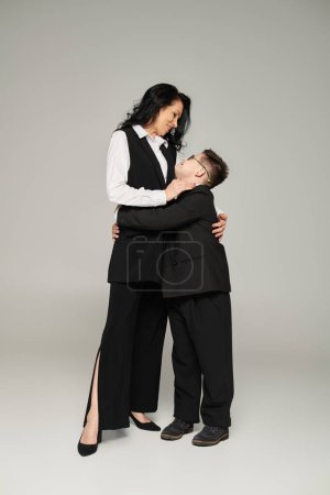 schoolboy with down syndrome and businesswoman hugging on grey, happy mother and son, special family