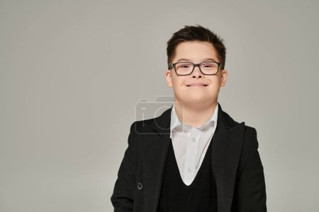 carefree schoolboy with down syndrome and genuine smile looking at camera on grey,  portrait