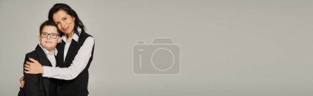 Téléchargez les photos : Femme d'affaires étreignant son fils avec le syndrome du duvet en uniforme scolaire sur gris, parent solidaire, bannière - en image libre de droit