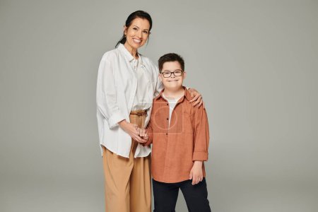 Téléchargez les photos : Femme d'âge moyen et fils avec le syndrome du duvet portant des vêtements élégants et tenant la main sur gris - en image libre de droit