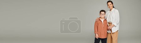 Téléchargez les photos : Élégant femme d'âge moyen et fils avec le syndrome du duvet souriant sur gris, amour et soins, bannière - en image libre de droit