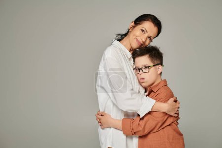 Photo for Joyful middle aged woman hugging son with down syndrome and smiling at camera on grey, banner - Royalty Free Image