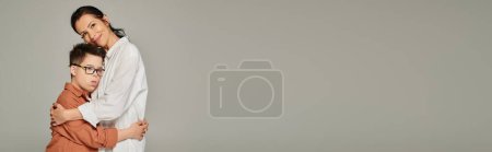 Téléchargez les photos : Femme mature et garçon avec le syndrome du duvet dans des vêtements élégants embrassant gris, bonheur, bannière - en image libre de droit