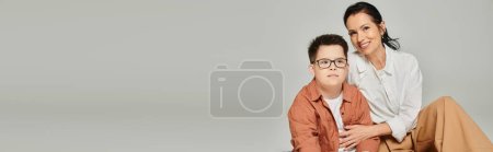 Téléchargez les photos : Femme d'âge moyen étreignant son fils avec le syndrome du duvet portant des lunettes sur gris, bannière, espace de copie - en image libre de droit