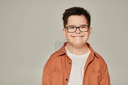 portrait of joyful boy with intellectual disability, in shirt and eyeglasses smiling on grey